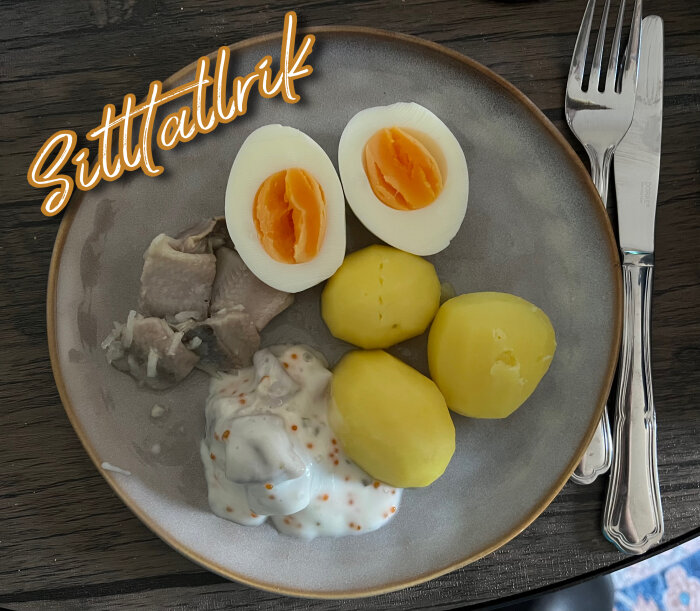 Tallrik med löksill, skärgårdssill, kokt potatis, halverade ägg och hårt bröd vid sidan, bestick bredvid. Text "Sittatlrik" syns ovanför.