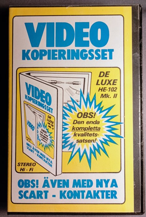 Förpackning av ett VHS-kopieringsset, "De Luxe HE-102 Mk. II", med text om kompletta kvalitetssatsen och SCART-kontakter.