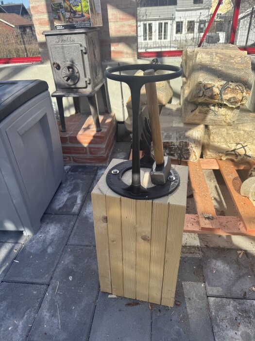 Vedklyv på träblock bredvid liten kamin och staplat virke i verkstadsmiljö.