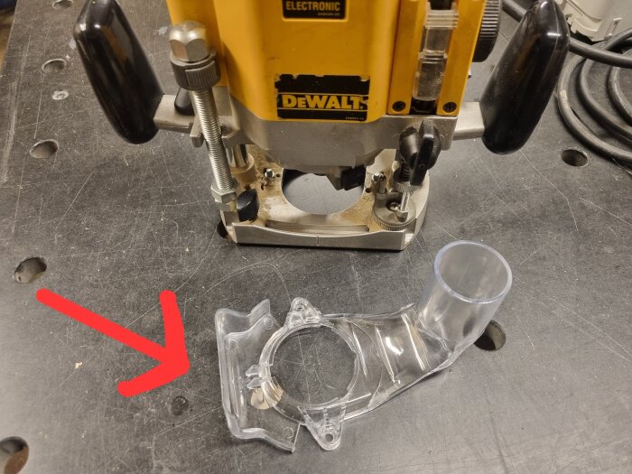 Plastdel för Dewalt-verktyg på arbetsbänk, markerad med en röd pil.