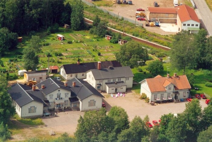 Flygfoto av stor fastighet med flera byggnader, grönområden och parkeringsplats i Krylbo, Avesta.