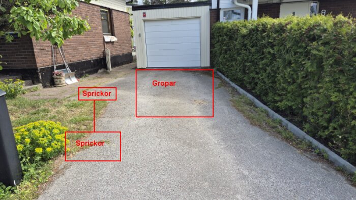 En uppfart i behov av reparation, med sprickor i asfalten nära gröna växter och en garageinfart där gropar är markerade.