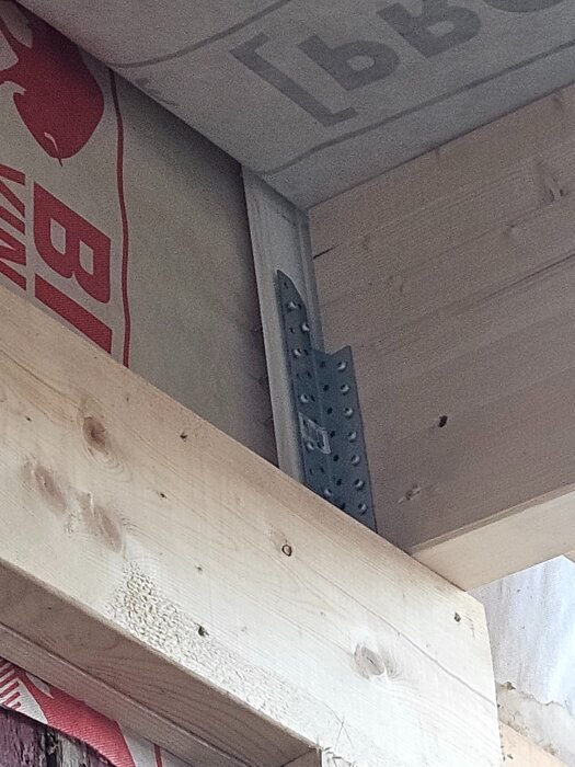 Byggkonstruktion med träpanel, plåt och en balksko som syns delvis under ett tak, med isolering bakom.