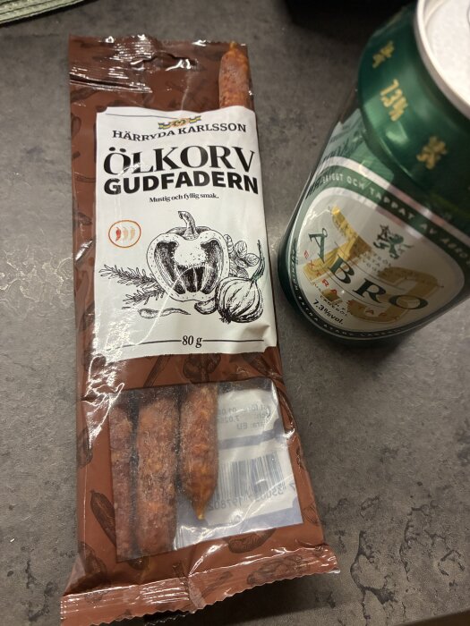 Förpackning med ölkorv Gudfadern och en burk Åbro öl på ett grått bord.