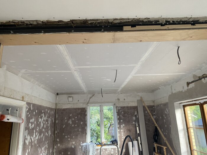 Rum under renovering med gipsplattor monterade på taket och väggar i behov av förarbete. Verktyg och material syns i bakgrunden.