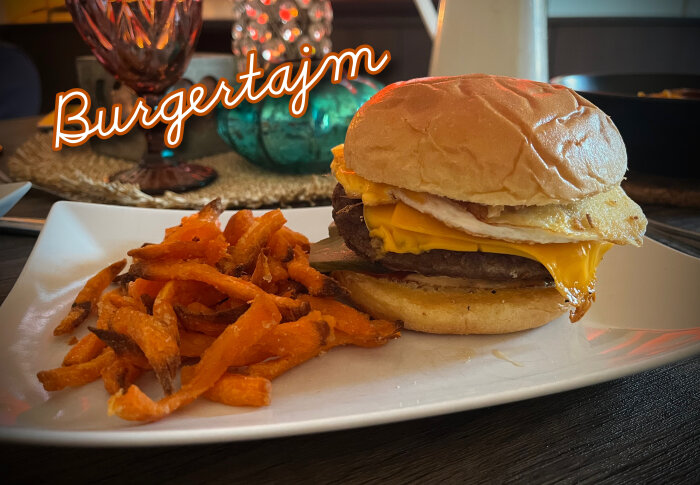 Burger med ost och ägg på en tallrik tillsammans med sötpotatispommes. Ordet "Burgertajm" står i förgrunden.