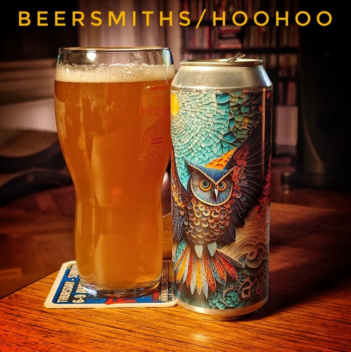 Ett glas öl på ett bord bredvid en burk med en färgglad uggla på etiketten. Texten "BEERSMITHS/HOOHOO" syns ovanför.