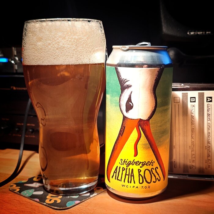 Ett glas öl bredvid en burk med etiketten "Stigbergets Alpha Boss WCIPA 7.0%" på ett bord.