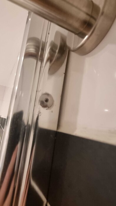 Metallfäste på badrumsvägg med två små hål, eventuellt från tidigare glasvägg, där användaren vill ta bort utan att skada kaklet.