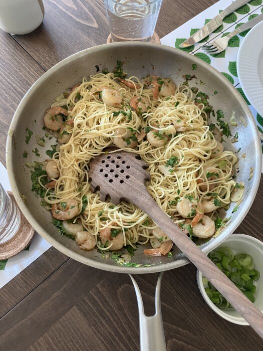Citronpasta med räkor, vitlök och chili i en stekpanna med en tallrik grön lök vid sidan.