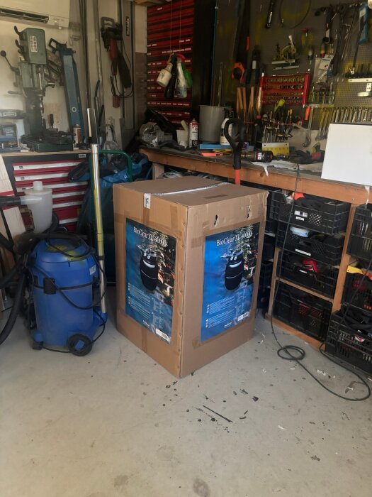 Stor kartong märkt "BioClear XL-40000" i ett välfyllt garage med verktyg och utrustning.