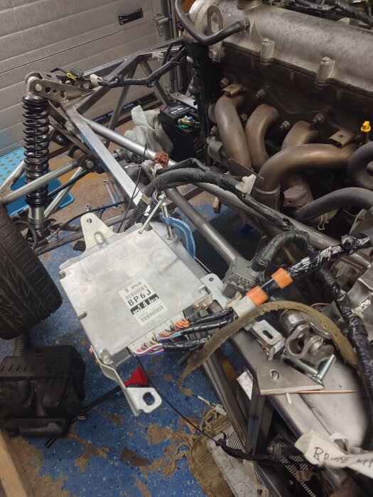 Chassi med motor och ledningar, synligt oljefilter och pumpanslutningar, diverse kopplingar och kablar på ett garagegolv.