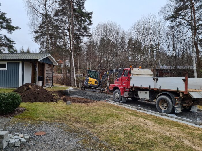 Grävmaskin och lastbil vid ett hus, jordhög och förberedelse för mur och trappsteg i en trädgård.