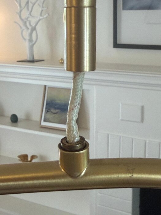 Närbild av en trasig koppling på en taklampa i mässing, med synlig vajer och omgivande vit inredning i bakgrunden.