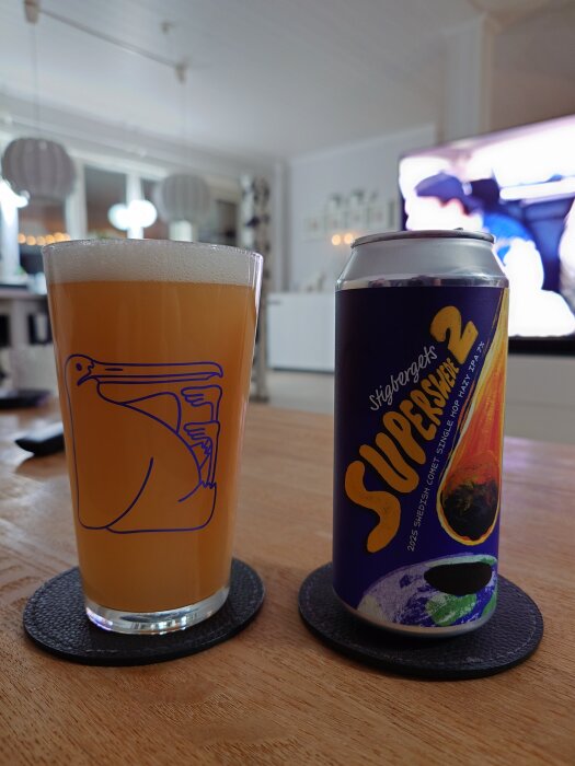 Ett glas med ljus öl bredvid en burk Stigbergets Superswell 2 IPA på ett bord i vardagsrum.