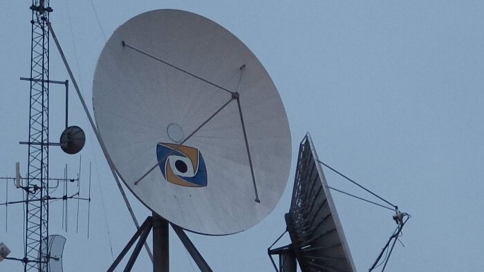 Satellitdiskar och antenner på en mast mot en blå himmel.