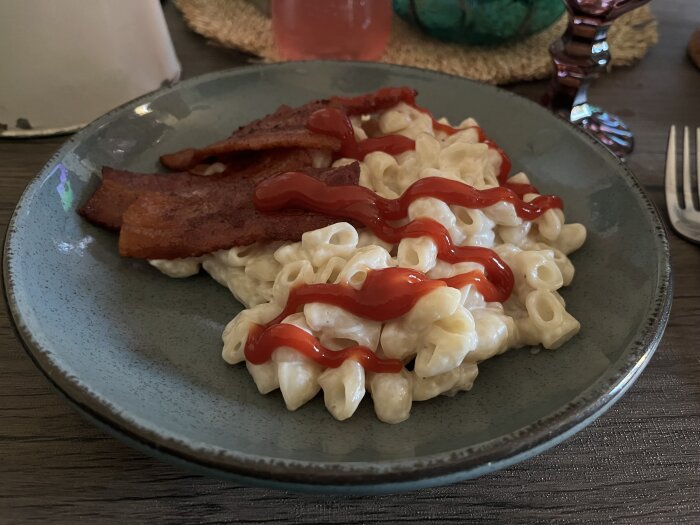 Stuvade makaroner med ketchup och stekfläsk på en tallrik.