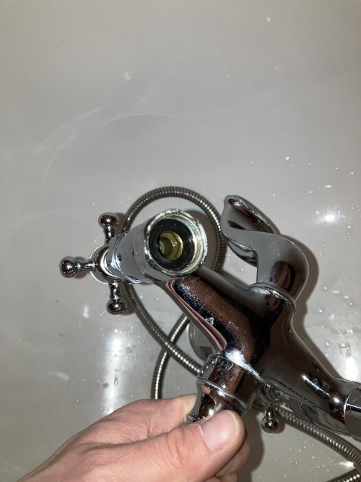Kromad badkarsblandare med synlig slang och problematiskt dräneringshål. Användarens hand håller i fästet där läckage uppstår.