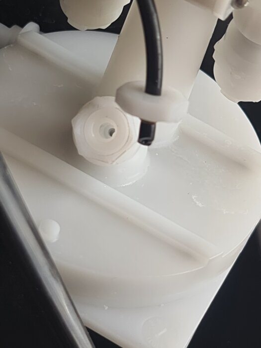 Närbild av en trasig slangkoppling i en kolsyremaskin, vit plastdel med svart kabel utstickande.