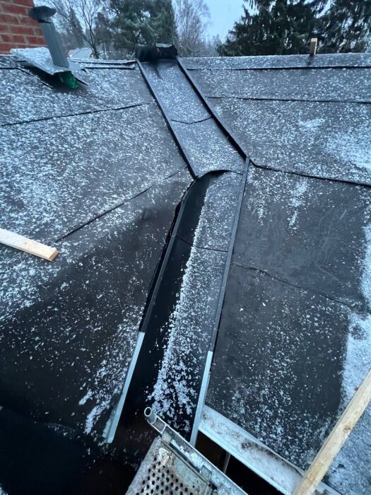 Tak med snö, synliga vinkelrännor och takpapp. Utsikter för bristfällig installation på grund av dåligt limmad papp och potentiellt felaktigt monterade rännor.