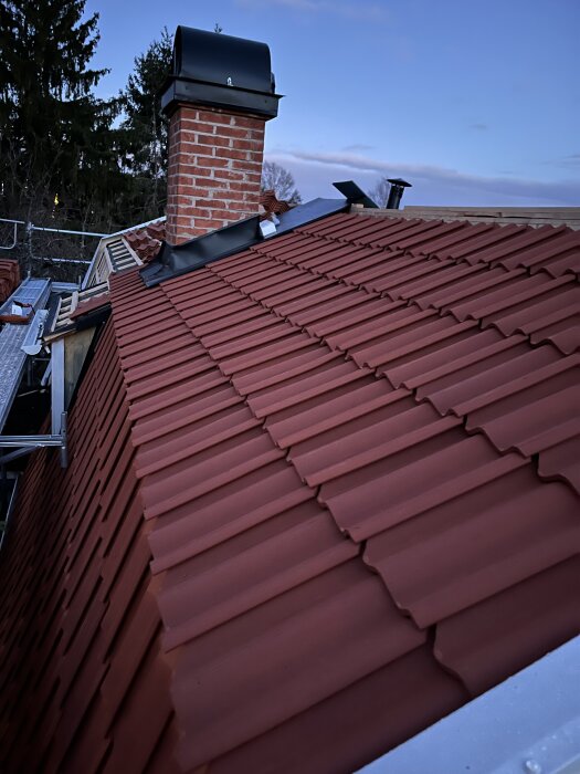 Tak med nya tegelpannor, skorsten och takkonstruktion med ventilationsstos, fotograferat vid gryning eller skymning.