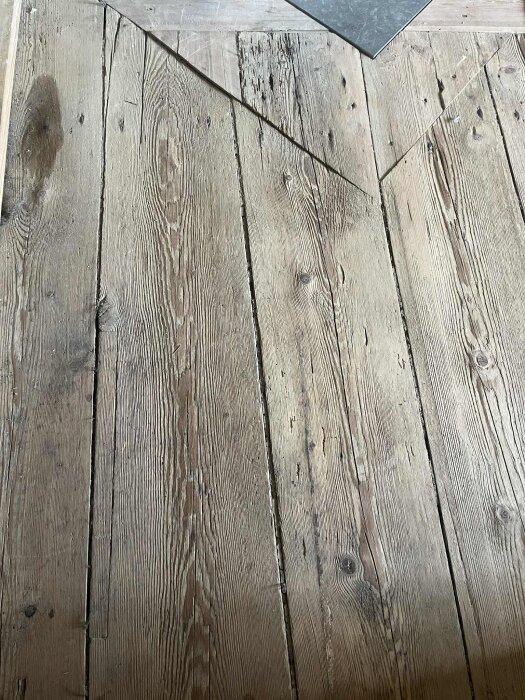 Gammalt trägolv från 1800-talet med smidda spikar, ser torrt och poröst ut med synliga sprickor och ojämn yta.