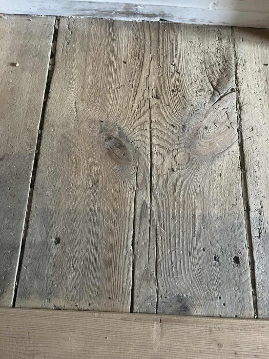 Gammalt, slitet trägolv med sprickor och ojämnheter, spikat med smidda spikar. Golvbrädorna ser torra och porösa ut.