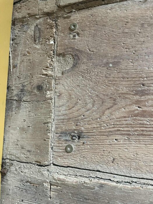 Gammalt trägolv med slitage och smidda spikar, visar ojämn och sprucken yta.