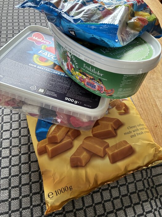 Flera förpackningar med olika slags godis, inklusive fruktgodis och kola, ligger staplade på ett bord med rutigt mönster.