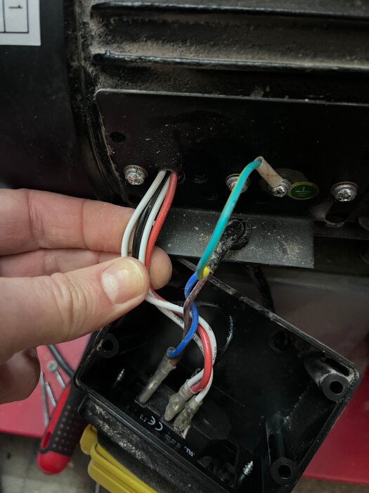 Hand som visar kablar anslutna till motorhus, inklusive röd, vit, blå och grön/gul kabel i en spånsugsmaskin.
