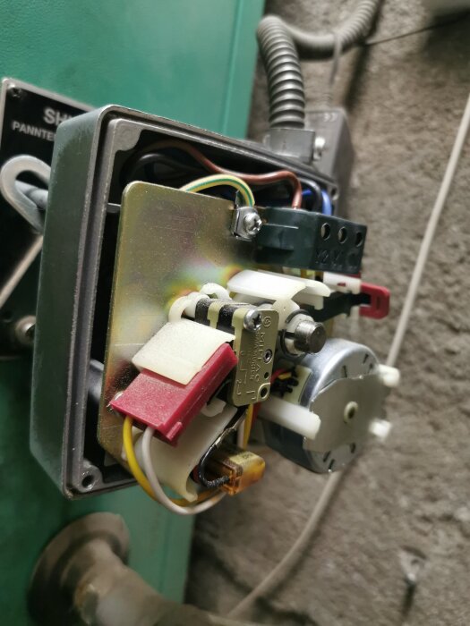 En närbild av en elektronisk apparat med flera färgade kablar och en metallplatta, tagen från sidan i vad som verkar vara ett tekniskt utrymme.
