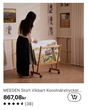 Kvinna står bredvid ett konstnärstryckställ med flera målningar, placerat i ett rum med konstverk på väggarna.