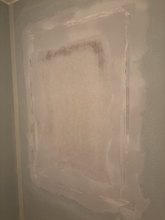 En spacklad vägg med ojämnheter och kanter synliga, delvis slipad för reparation.