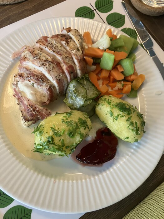 Kyckling inlindad i bacon på en tallrik med kokt potatis med persilja, blandade grönsaker och en klick sås.
