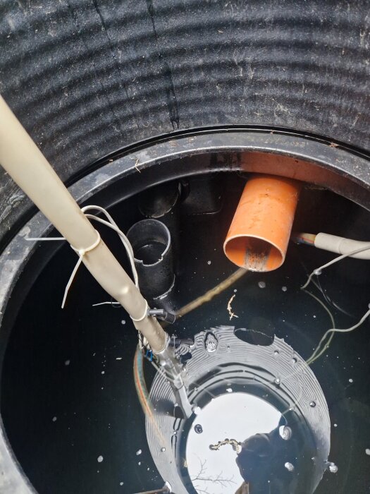Hemmabygd nivåmätare med sladdar och givare installerade i en vattenbehållare, ansluten till en orange rörledning.
