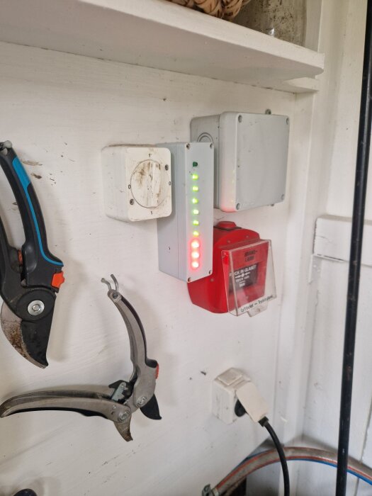 Hemmagjord nivåmätare med lysdioder monterad på väggen, omgiven av elboxar och verktyg som hänger på sidan.