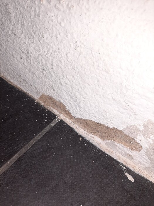 Flagig färg och exponerad puts i hörnet av en vägg i en skånelänga, där tidigare plastfärg börjat släppa.