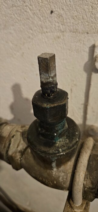 Avstängningsventil med korrosion och läckage upptill, märkt AHA SIS. Vattenrör i bakgrunden.
