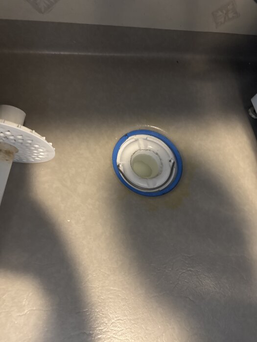 Nyinstallerat vitt vattenlås med blå tätning under diskbänk i tvättstuga, relaterat till avloppsluktproblem.