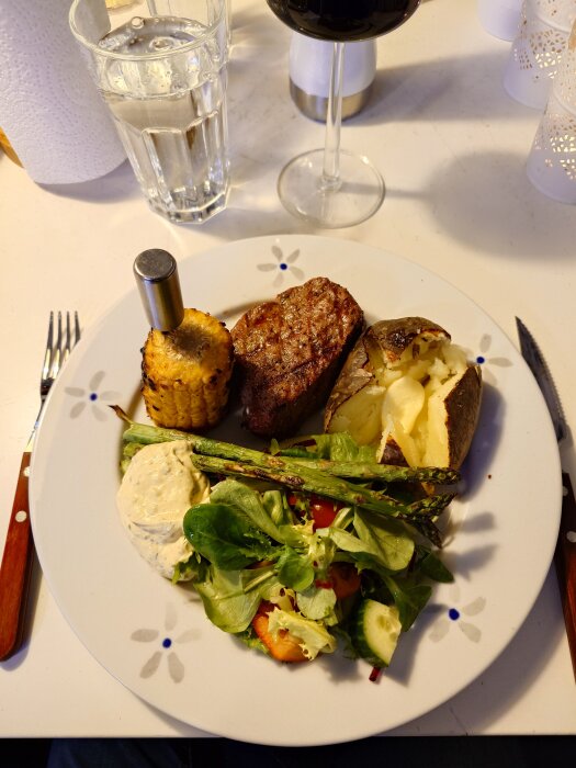 Bakad potatis, grillad oxfilé, majs, sparris och sallad på en vit tallrik.