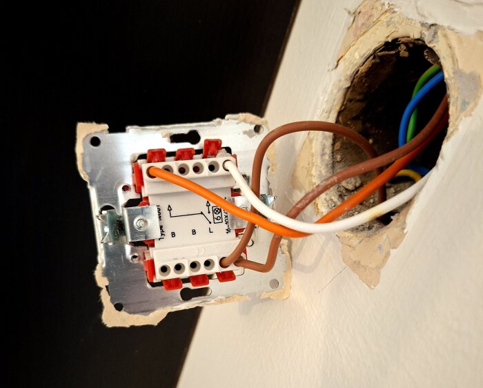 Elektrisk kopplingsdosa i vägg med flera färgade kablar anslutna; installation av dimmer kopplad till bruna, orange och vita sladdar.