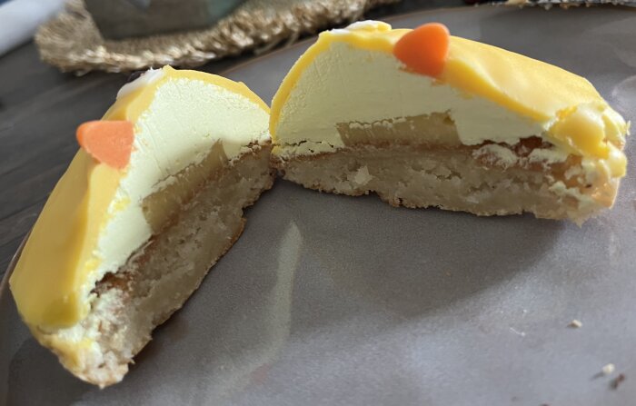 Delad citronbiskvi med gul glasyr och marsipan på en tallrik, dekorerad med små orange detaljer upptill.