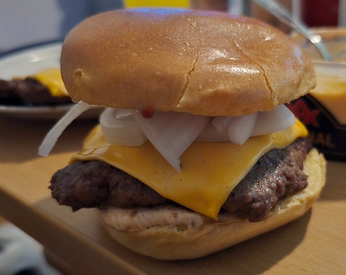 Hamburgare med cheddarost och lök på en brödskiva, serverad på ett bord.