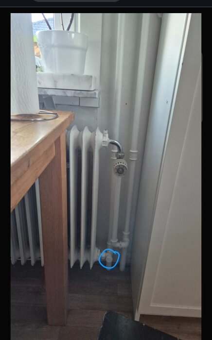 Radiator med röranslutning i kök, markerad med en blå cirkel, med frågeställning angående vattenburen golvvärme från radiatorsystemet.