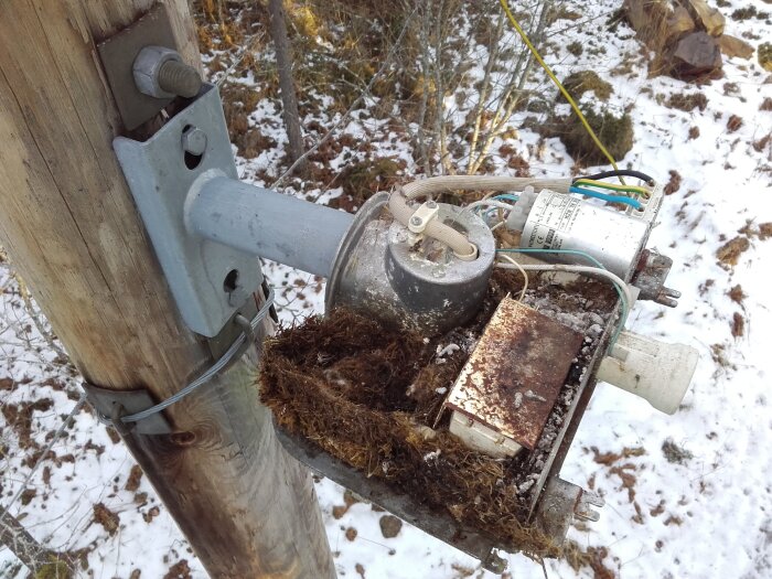 Markbunden drossel på stolpe omgiven av vinterlandskap, med kablar och elektriska komponenter synliga ovanpå.