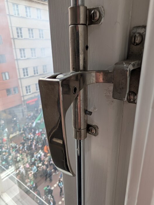 Fönsterhandtag med vertikal stång och synlig gängstång på gammalt fönster.