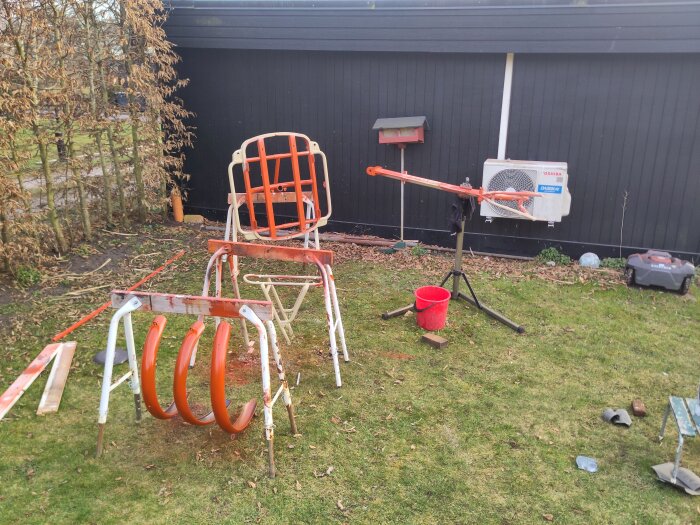 Delar av en lådcykel står ute på gräsmatta; ramen och andra delar är nyligen lackerade i orange, med en röd hink och verktygsställ bredvid.