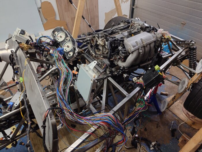 Motor och kablage i en bil, omgivna av instrumentpaneler och avbitartång, under ett bilmekanikprojekt.