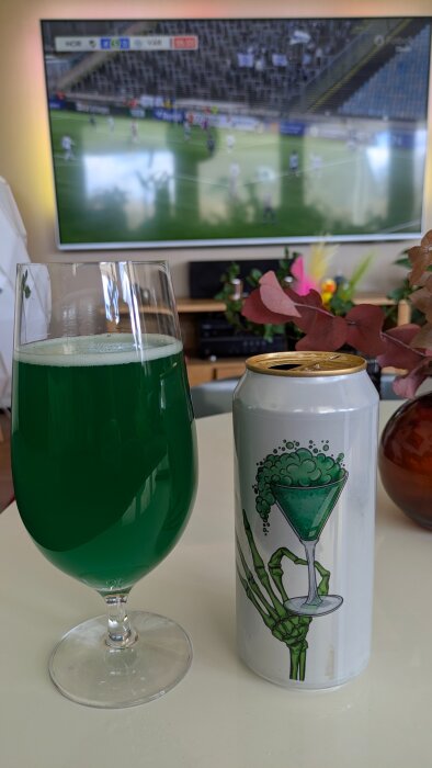 Grönt suröl från Fermenterarna i glas och burk på ett bord, med fotbollsmatch på TV i bakgrunden.