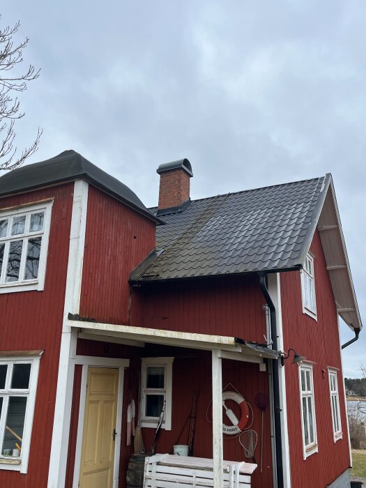 Rött sommarhus med två våningar, svart tak och skorsten, ingen arbetsplattform vid skorstenen.